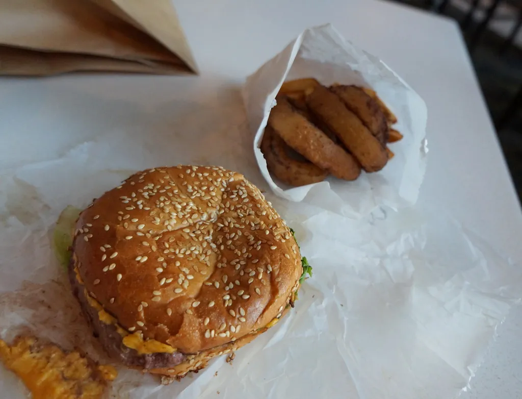 Bison Ralphie Burger with melted cheese on a sesame bun and onion rings at My Brother’s Bar in Denver
