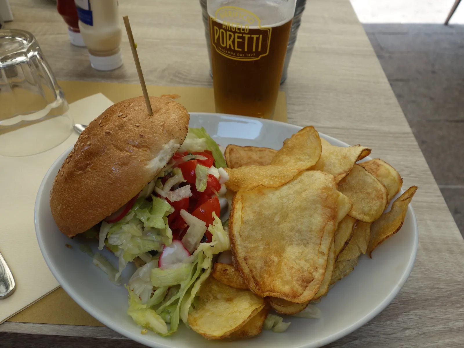 Best burgers in Milan: a hamburger on a sesame bun with lettuce, tomato and radish, with homemade potato chips and a beer on a Milan terrace