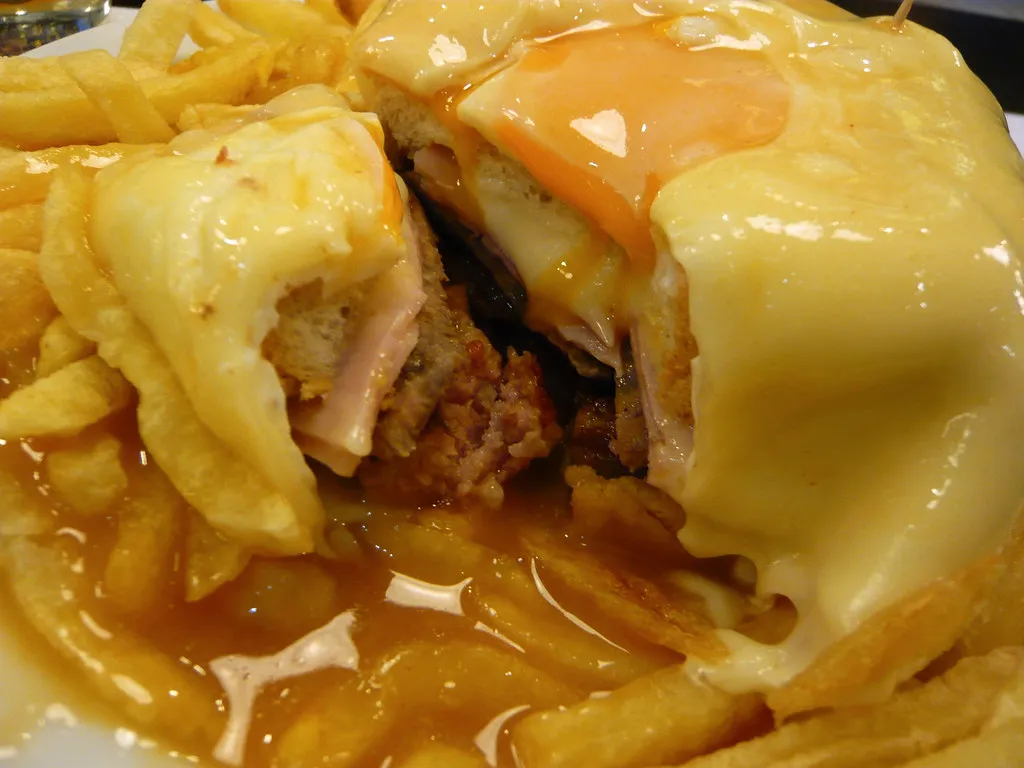 Corte de una francesinha de Oporto con huevo frito, salsa de cerveza y tomate y patatas fritas