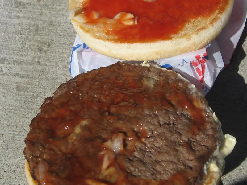 Inside a Hesburger hamburger: thin beef patty with chopped onion, a pickle slice, ketchup and mayonnaise, the base of the Hesburger cheeseburger