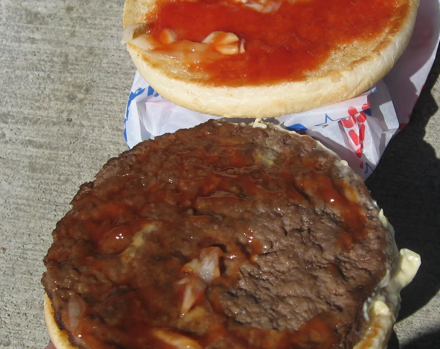Inside a Hesburger hamburger: thin beef patty with chopped onion, a pickle slice, ketchup and mayonnaise, the base of the Hesburger cheeseburger