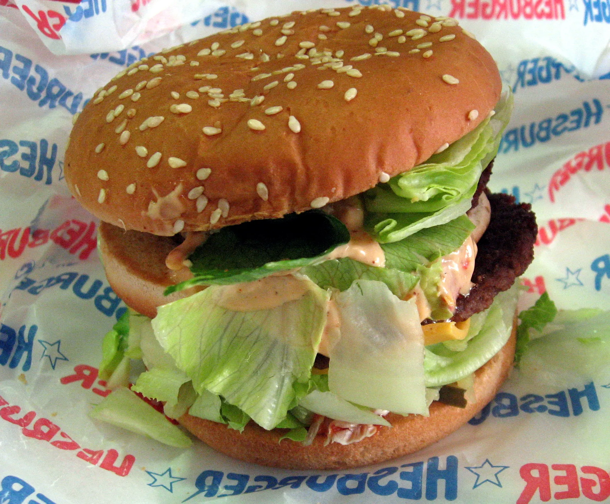 Hesburger burger on a sesame bun with lettuce, cheese and pinkish mayonnaise on the chain’s red-and-blue wrapper