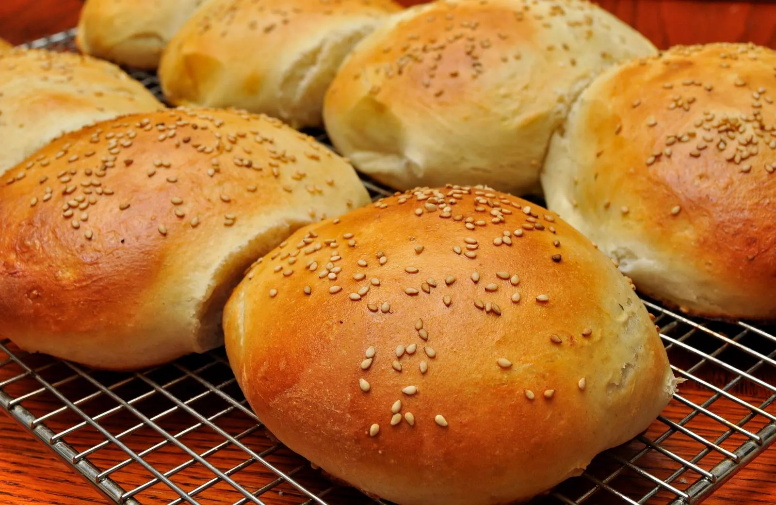 Golden homemade sesame burger buns cooling on a wire rack after baking