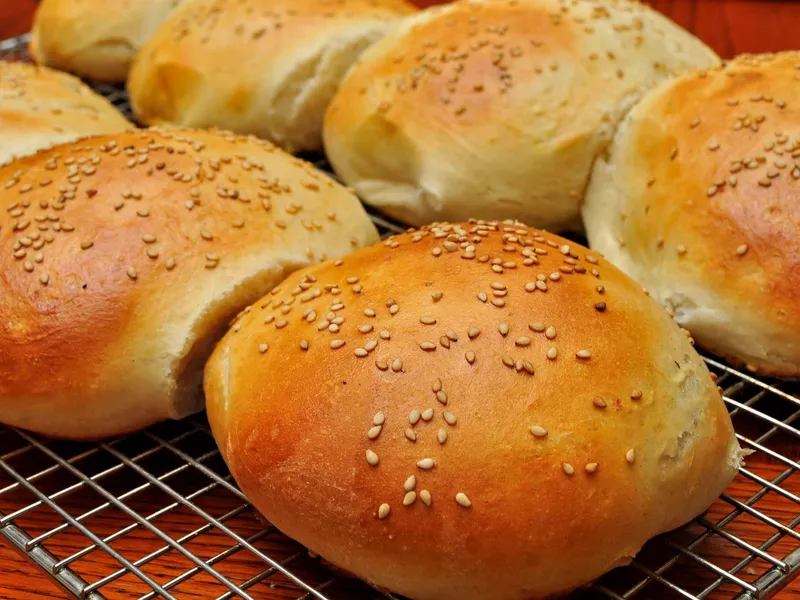 Golden homemade sesame burger buns cooling on a wire rack after baking