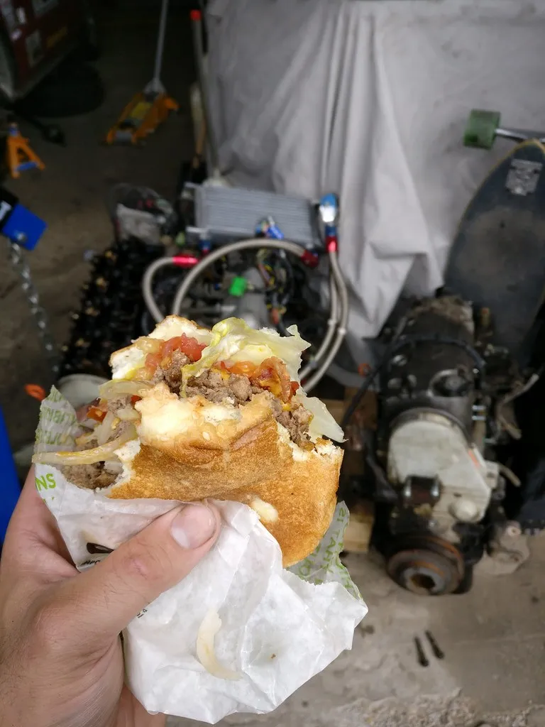 Half-eaten A&amp;W Teen Burger in its paper wrapper, showing the beef patty, lettuce, tomato and onion on a toasted bun