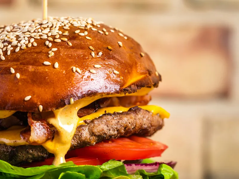 Homemade bacon cheeseburger on a toasted sesame seed bun with melted cheese, creamy sauce, tomato, red onion and lettuce, close to the A&W Teen Burger copycat build