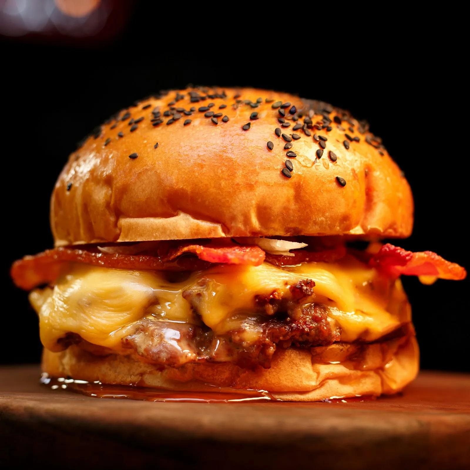 Bacon cheeseburger with cheese melted over a seared beef patty and crisp bacon on a black-sesame bun on a wooden board
