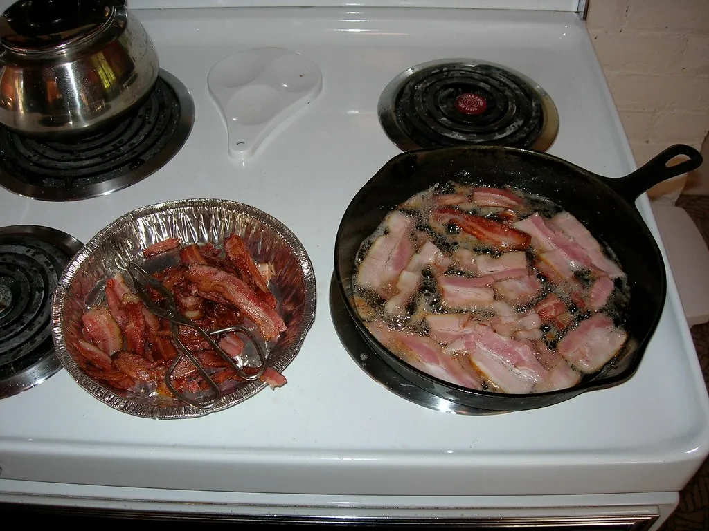 Crisp bacon slices draining next to a cast-iron skillet of bacon for two Bacon King copycat burgers