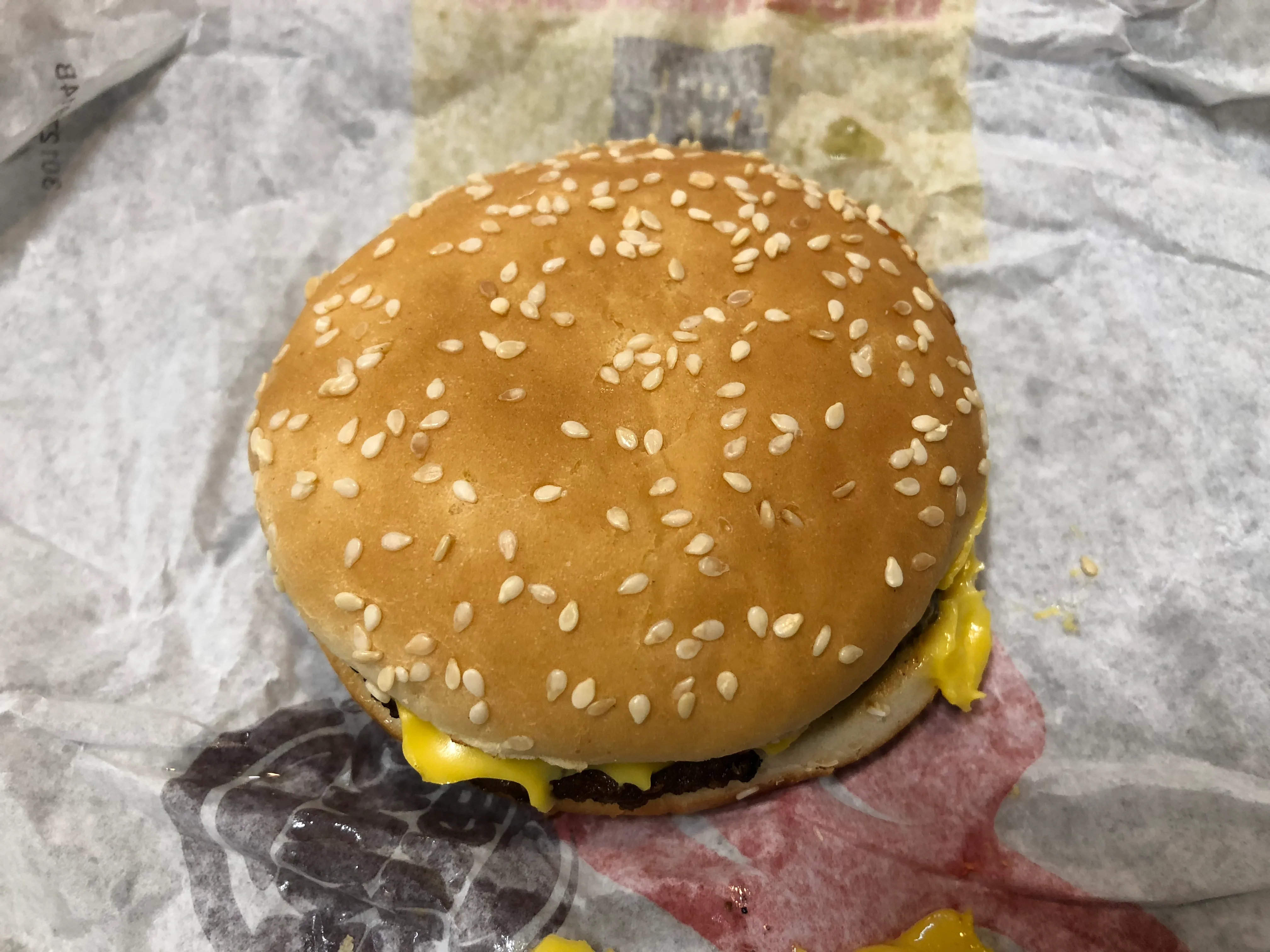 Top view of a Burger King cheeseburger with melted American cheese running out from under the sesame bun