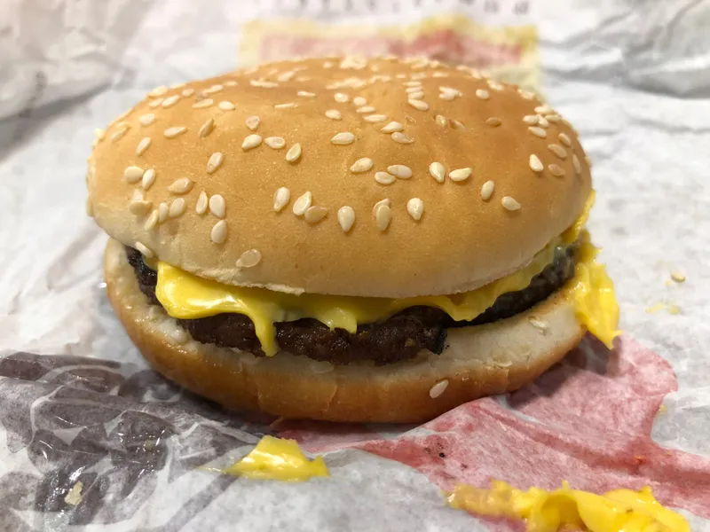 Cheeseburger Burger King d'origine grillé à la flamme, avec fromage fondu et pain au sésame, posé sur son papier d'emballage