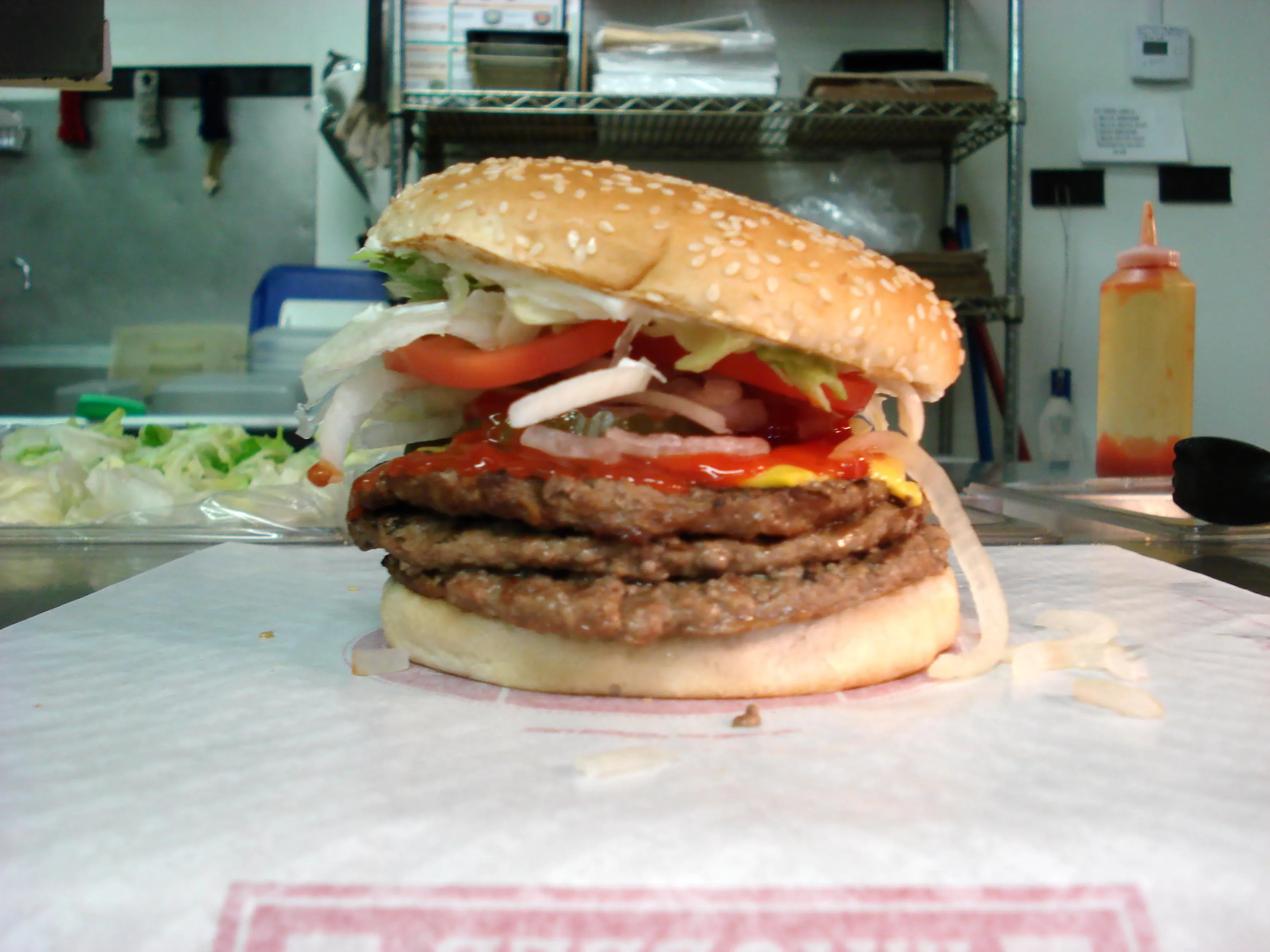 A Burger King Whopper with cheese assembled in the restaurant just before wrapping, with stacked cheesed patties and the cold toppings on top (triple version shown)