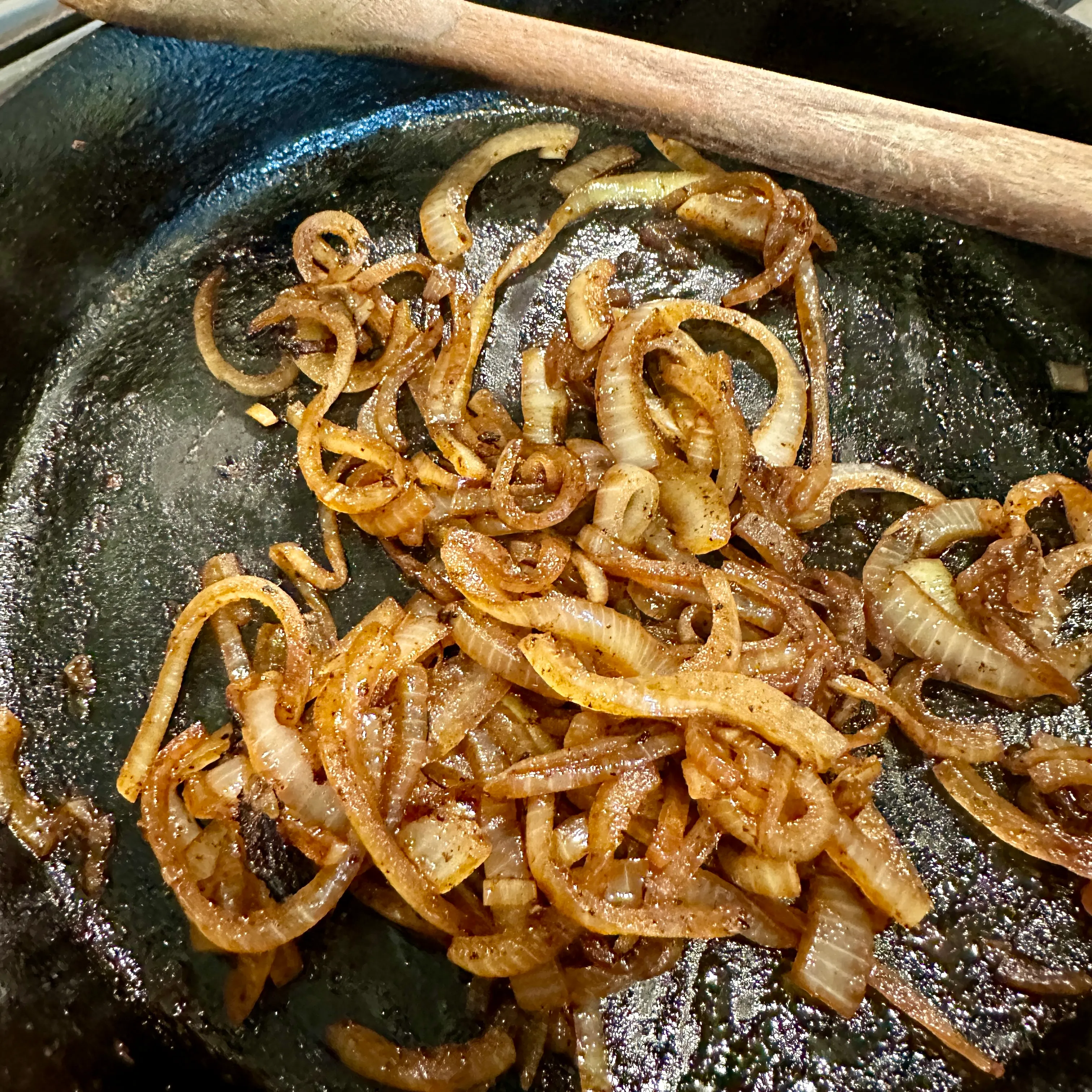 Onion rings softening in butter in a cast-iron skillet, browned at the edges, for a homemade patty melt