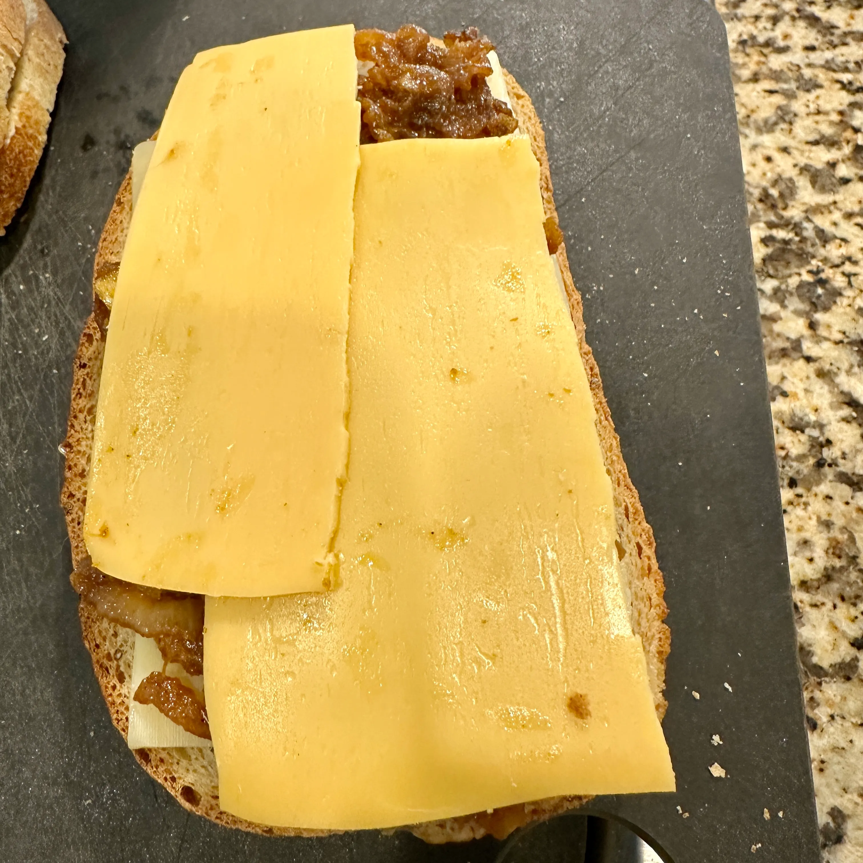 Homemade patty melt being assembled on sliced bread with cheese, grilled onions and a griddled beef patty
