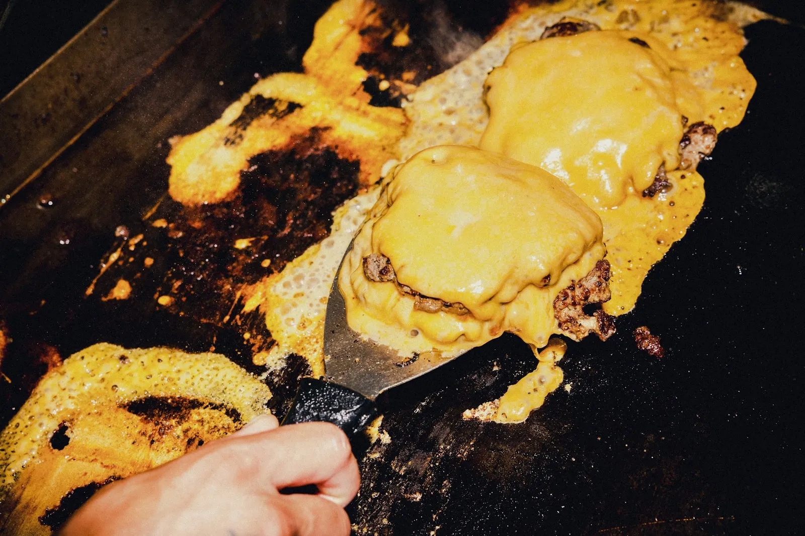 Slices of American cheese melting over thin smashed beef patties on a griddle
