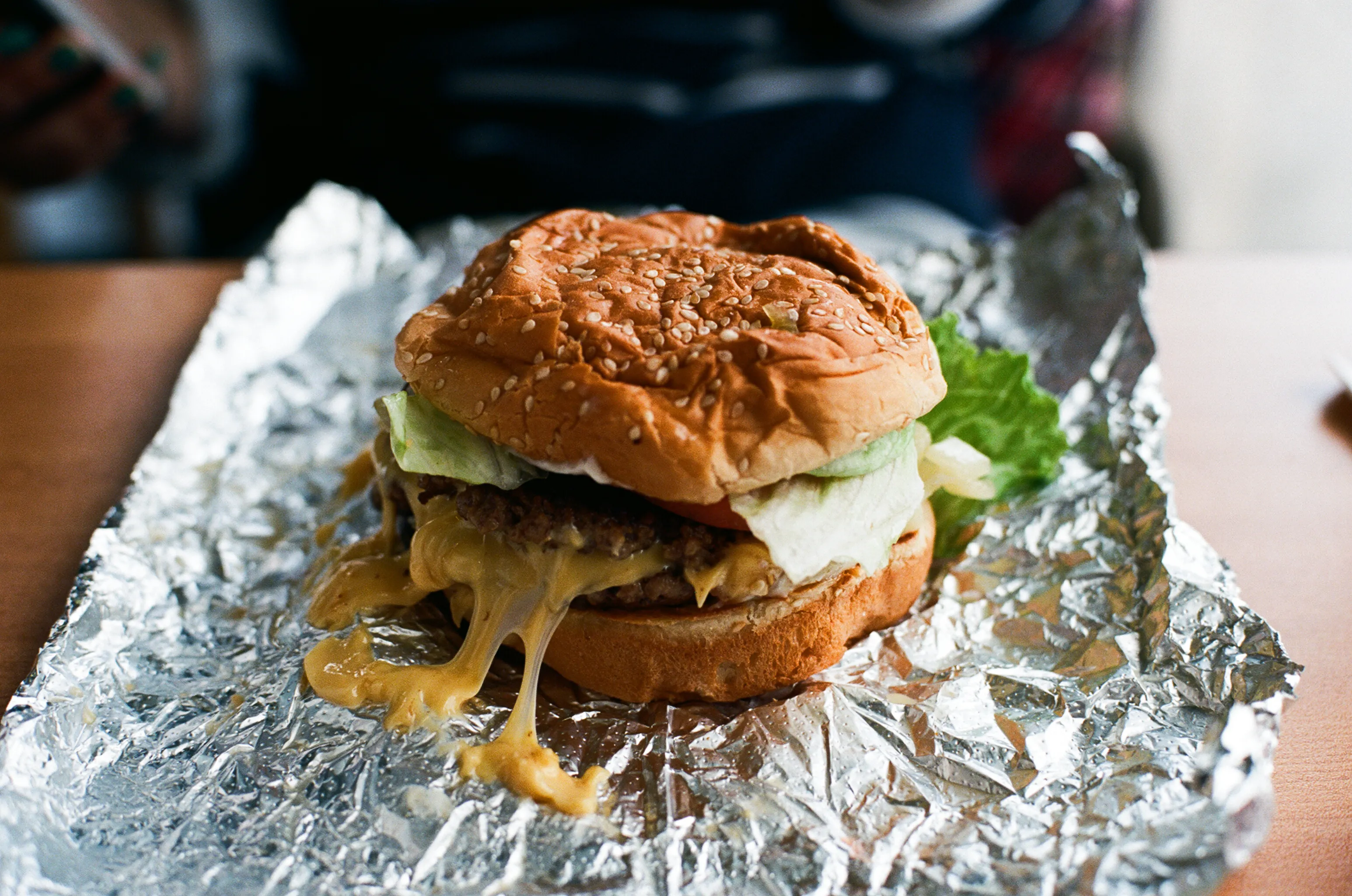 Five Guys double burger on its opened aluminum foil with two thin patties, lettuce and tomato on a toasted sesame bun