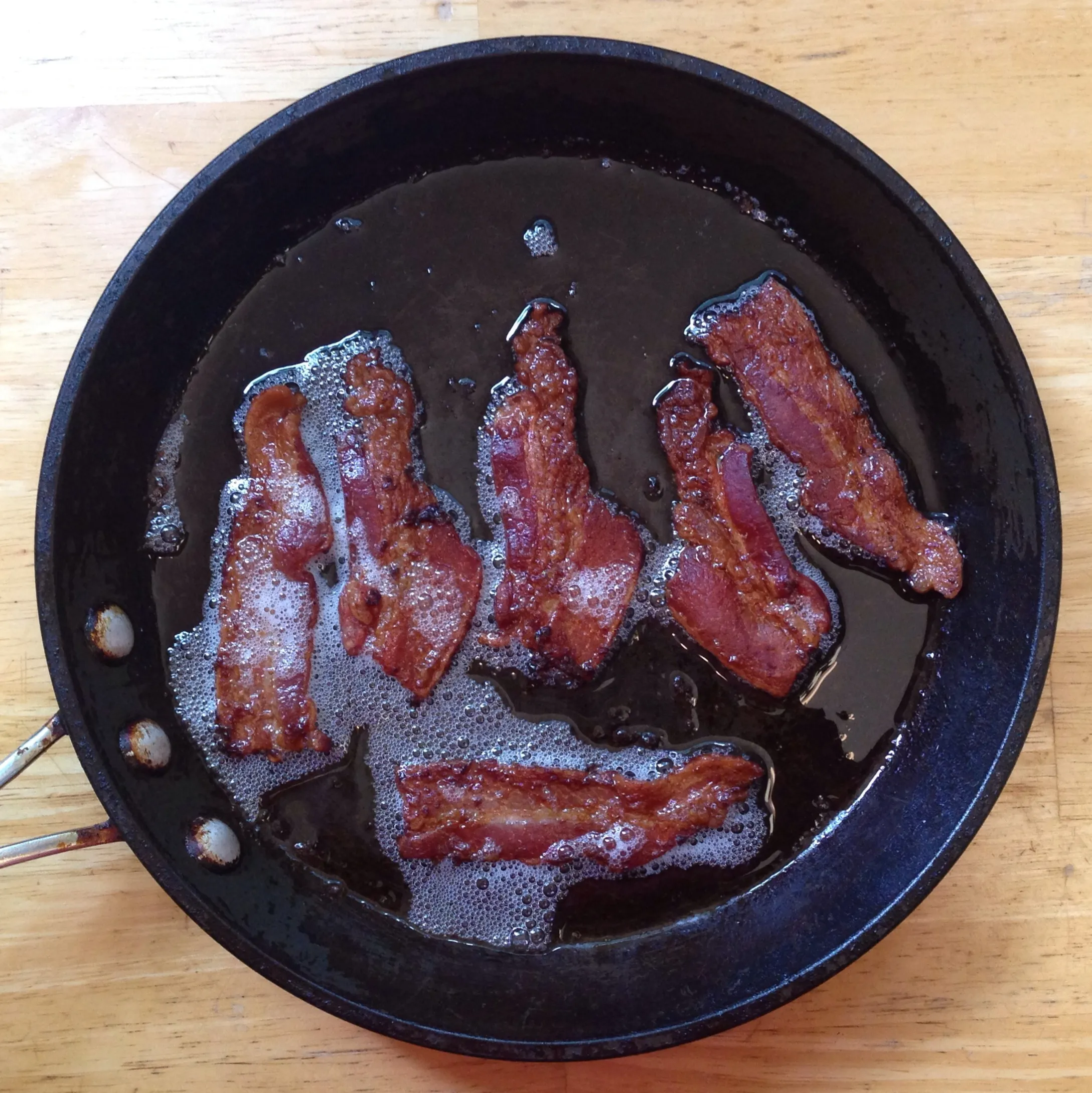 Bacon strips crisping in their own fat in a skillet for a homemade Five Guys Bacon Cheeseburger