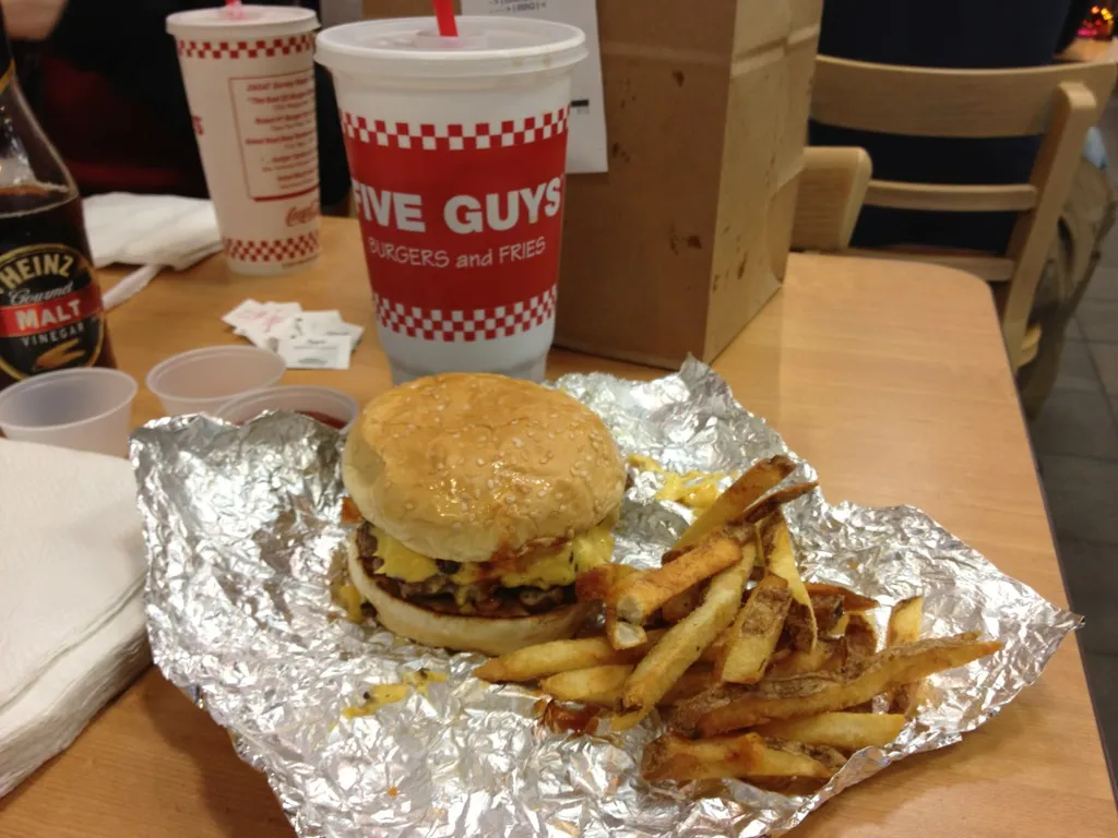 Five Guys bacon cheeseburger just unwrapped from its foil, cheese melted between the patties, next to fries