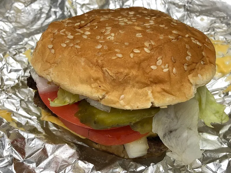 Cheeseburger Five Guys posé sur sa feuille d'aluminium : deux steaks, fromage américain fondu, salade, tomate, pickles et oignon dans un pain au sésame, l'original de cette recette maison