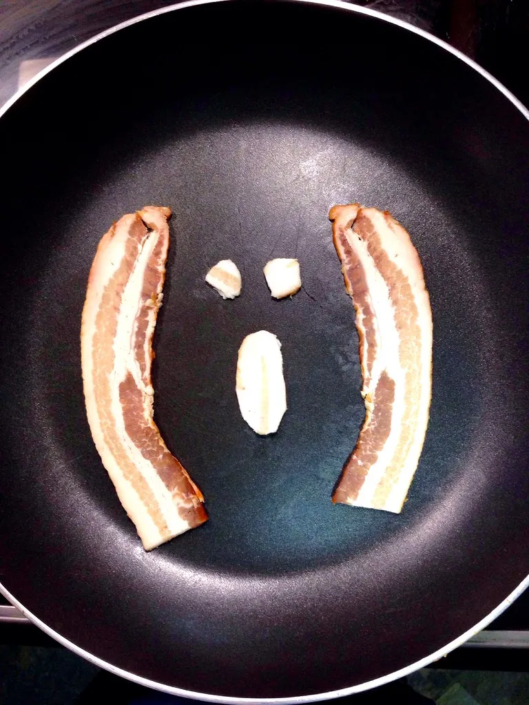 Two raw bacon strips in a cold skillet before cooking, the first step for crisp bacon in a Five Guys Little Bacon Burger copycat