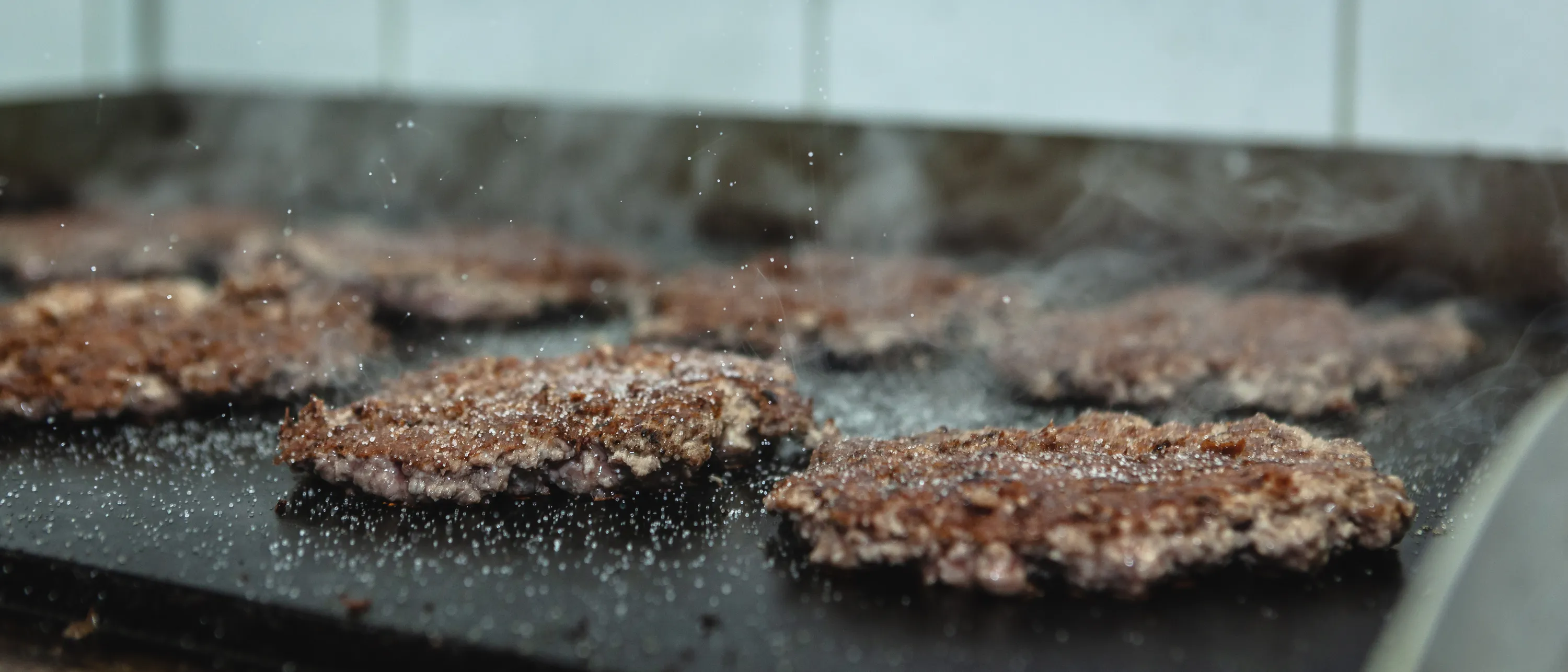 Thin pressed burger patties with a browned crust after the first flip on a hot griddle