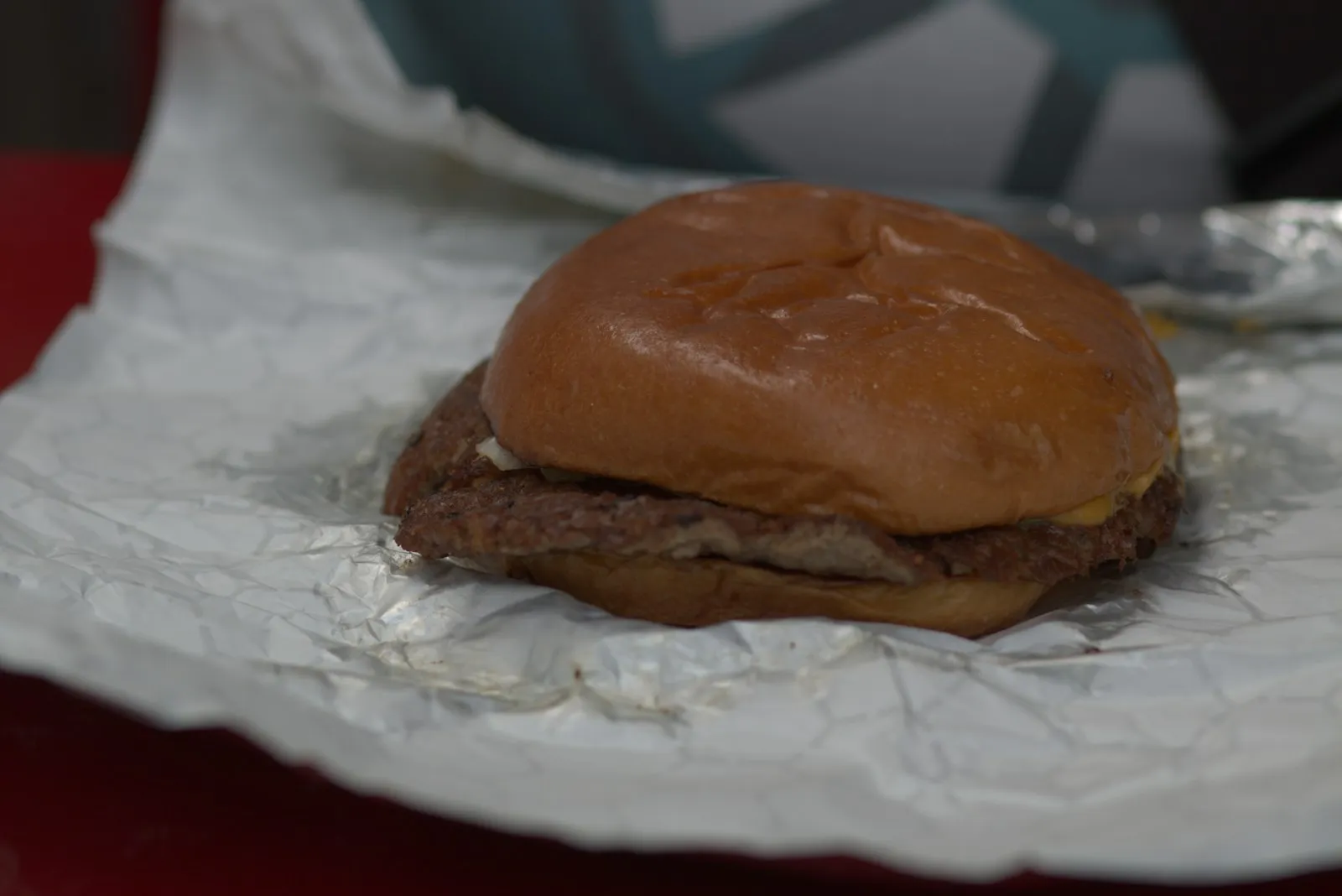 Single-patty cheeseburger on a toasted bun resting on aluminum foil before being wrapped, Five Guys style