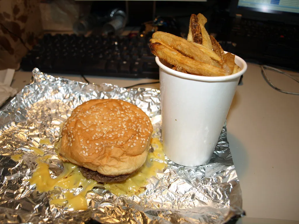 Five Guys cheeseburger unwrapped from its foil next to fries and the brown paper bag