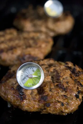 Thick beef patty grilling on hot griddle with thermometer checking well-done temperature
