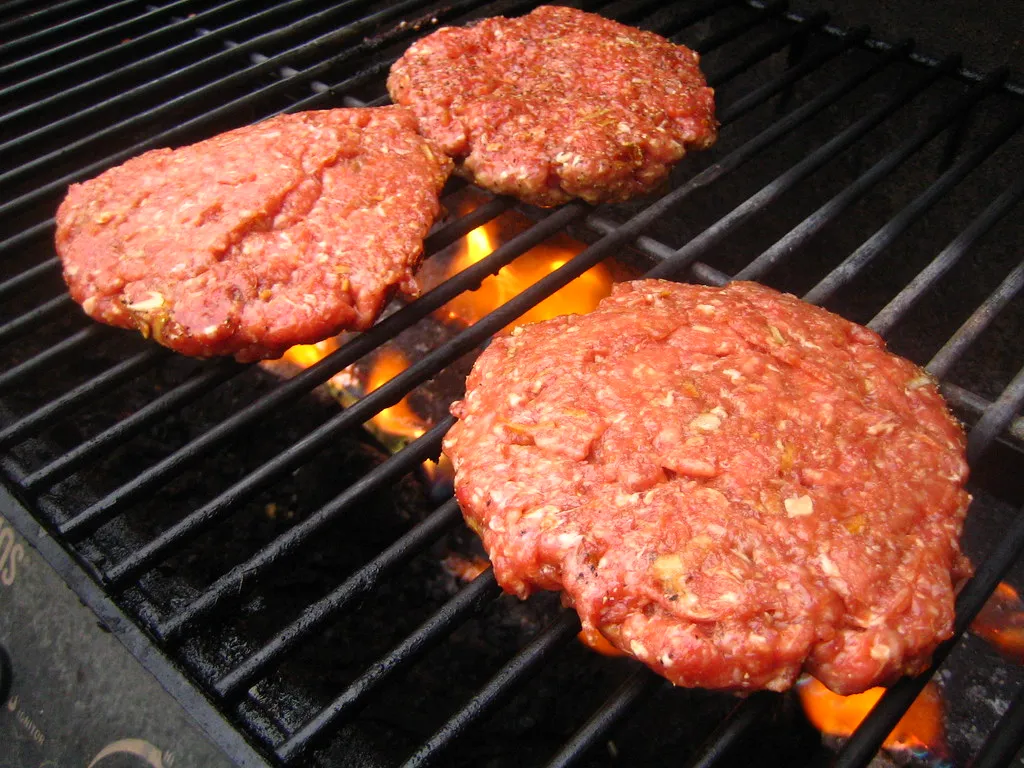 Beef patties grilling over direct flame, showing charred edges for flame-kissed method at 250-290°C