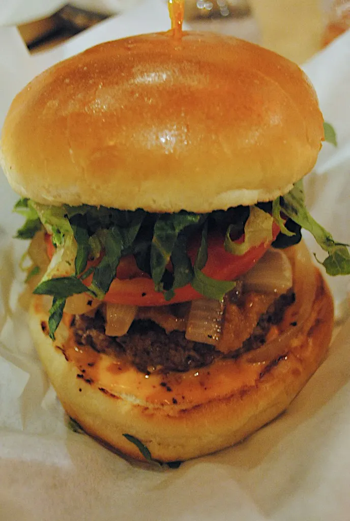 Stacked burger cross-section with beef, tomato, lettuce and onion on toasted bun, showing layer order