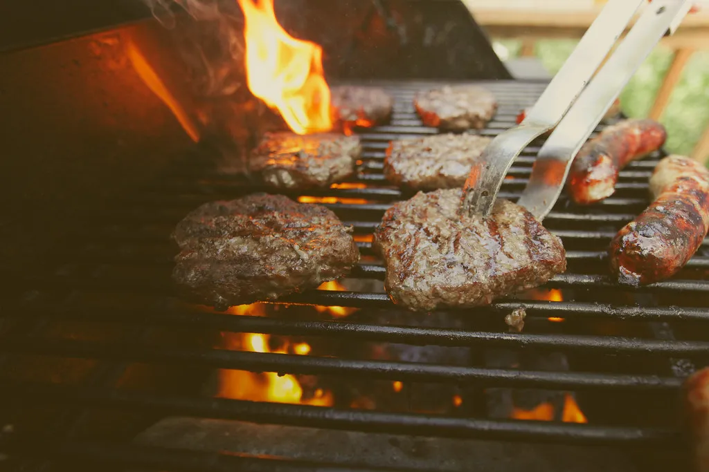 Beef patties flame-grilling over open flames on a barbecue grill