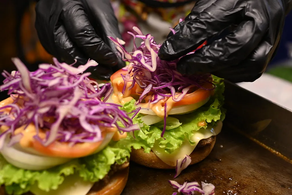 Assembling a Double Whopper with mayo, ketchup, pickles, onion, lettuce and tomato