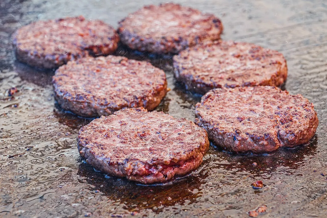 Six steaks hachés qui dorent dans leur graisse sur une plancha, la cuisson d’un Jumbo Jack maison