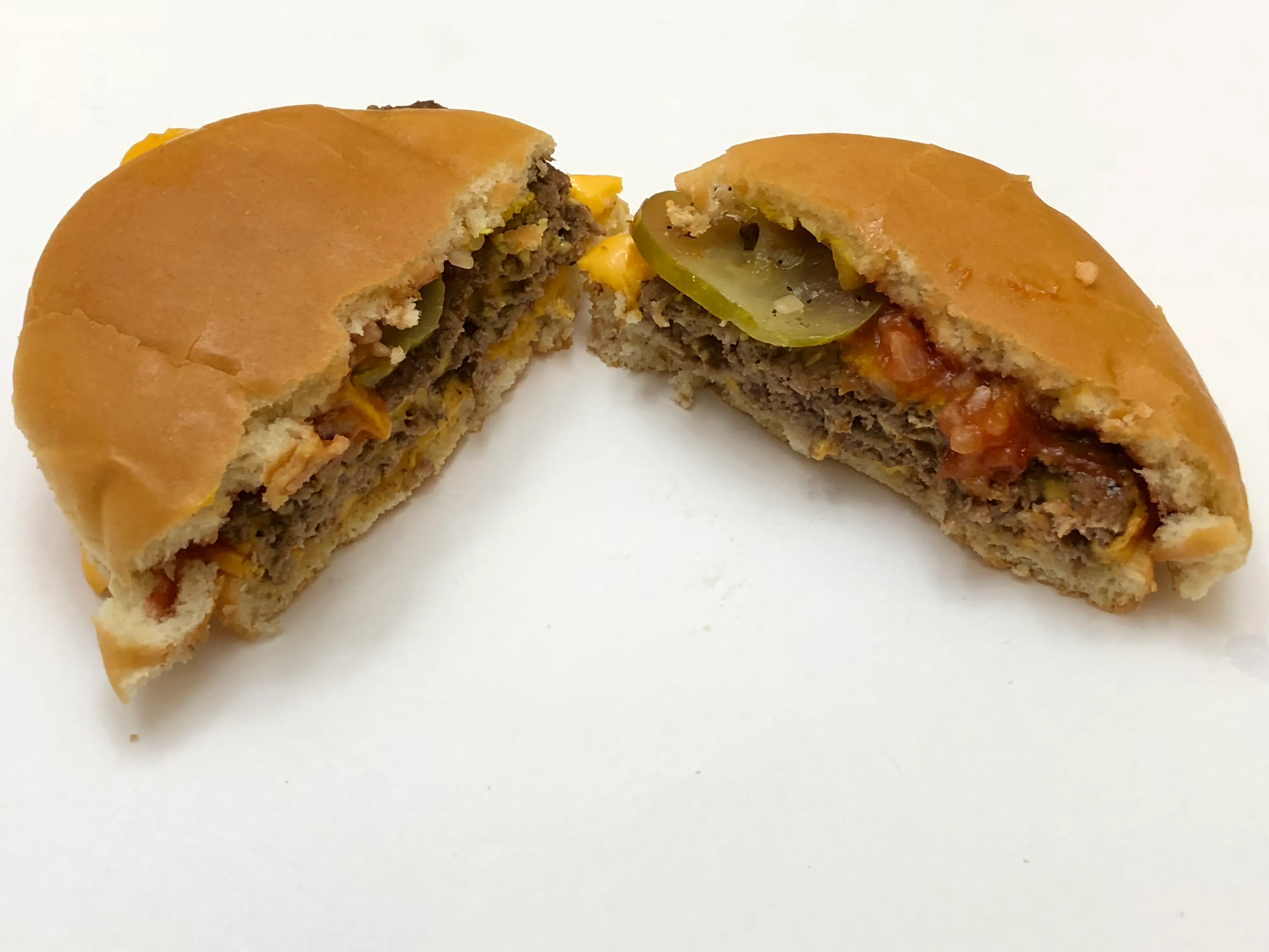 McDonald’s Double Cheeseburger cut in half showing two thin patties, a dill pickle chip, rehydrated onions, ketchup and mustard