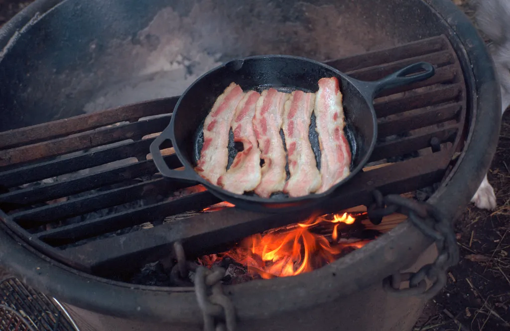 Bacon slices crisping in a cast-iron skillet, the first cooking step before smashing the burger patties in the same pan