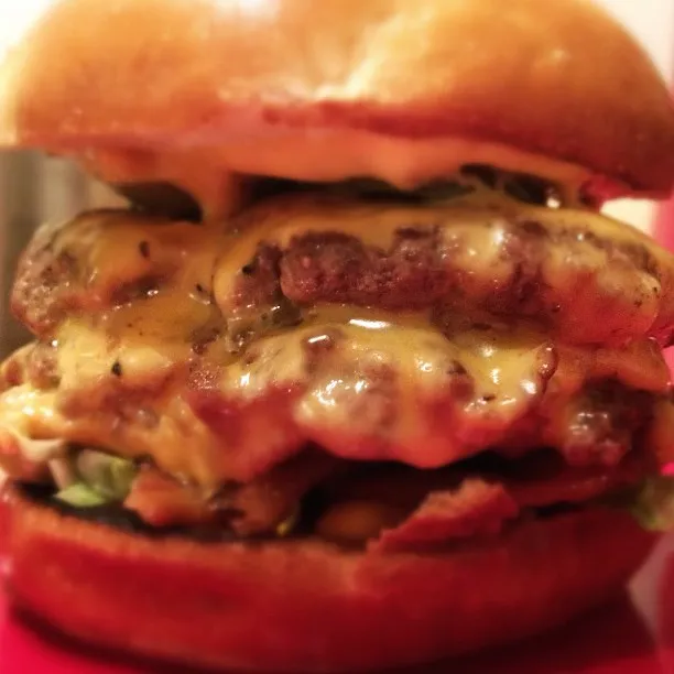 Double bacon cheeseburger close-up with two patties under melted cheese, bacon and lettuce