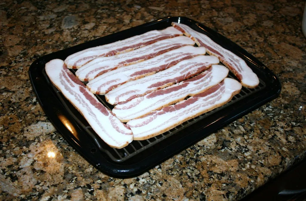 Raw bacon strips on a wire rack in a pan, ready to oven-crisp for a Sonic bacon double cheeseburger copycat