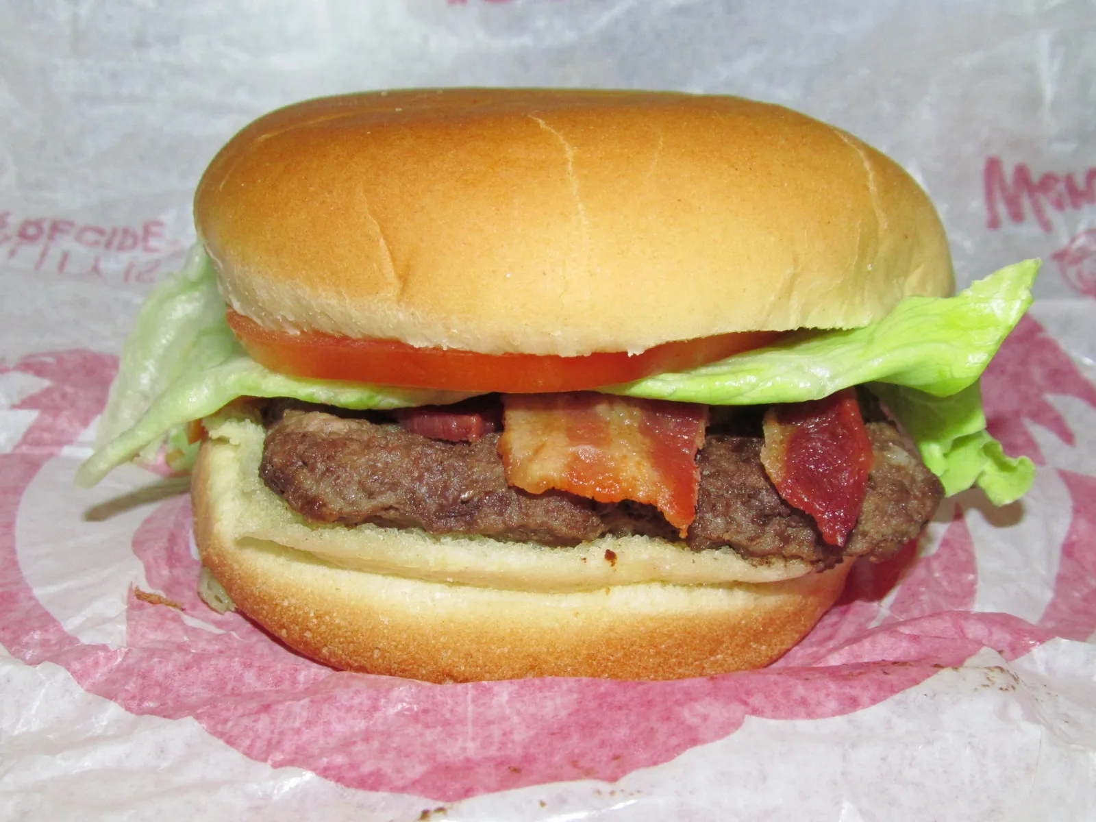 Side view of a Wendy’s Junior Bacon Cheeseburger showing a thin junior patty, bacon strips, lettuce and tomato