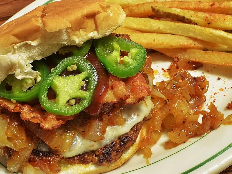 Bacon cheeseburger with melted cheese, grilled onions, glossy sweet and spicy sauce and green jalapeño on a soft white bun, styled like the Whataburger Sweet and Spicy Bacon Burger copycat