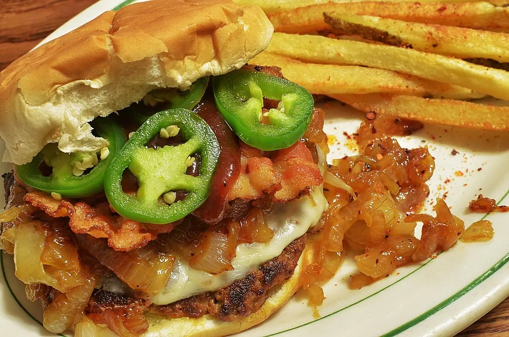Bacon cheeseburger with melted cheese, grilled onions, glossy sweet and spicy sauce and green jalapeño on a soft white bun, styled like the Whataburger Sweet and Spicy Bacon Burger copycat
