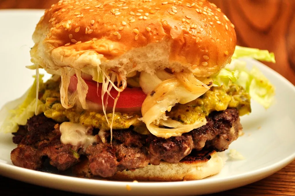 Stacked burger with lettuce, tomato, diced onions and pickles under a mustard-spread top bun, no cheese
