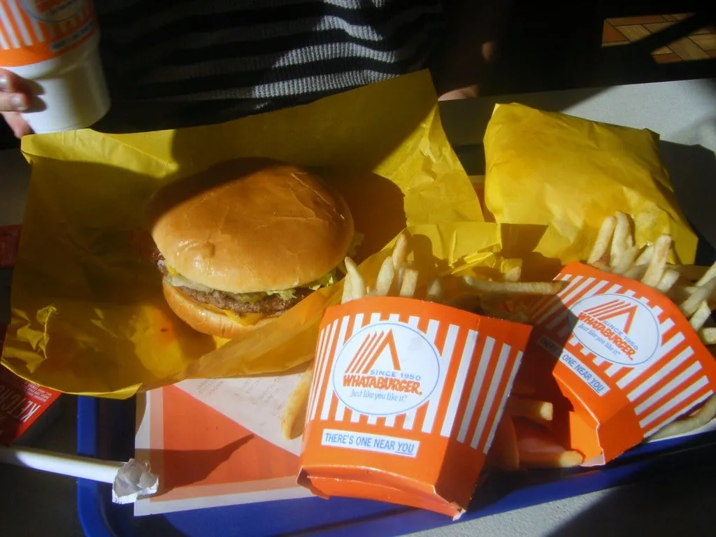 Whataburger au fromage sur son papier jaune et deux cornets de frites orange et blanc sur un plateau bleu, la commande de base chez Whataburger à Austin