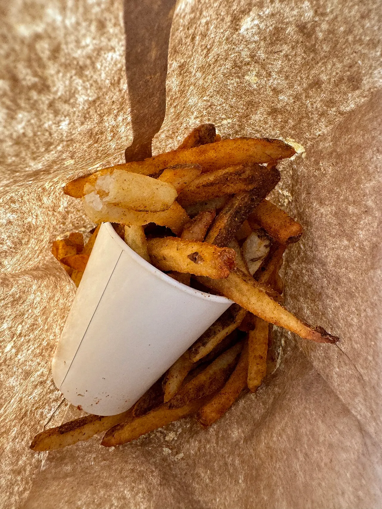 Five Guys Cajun fries spilling out of a paper cup into the brown takeaway bag