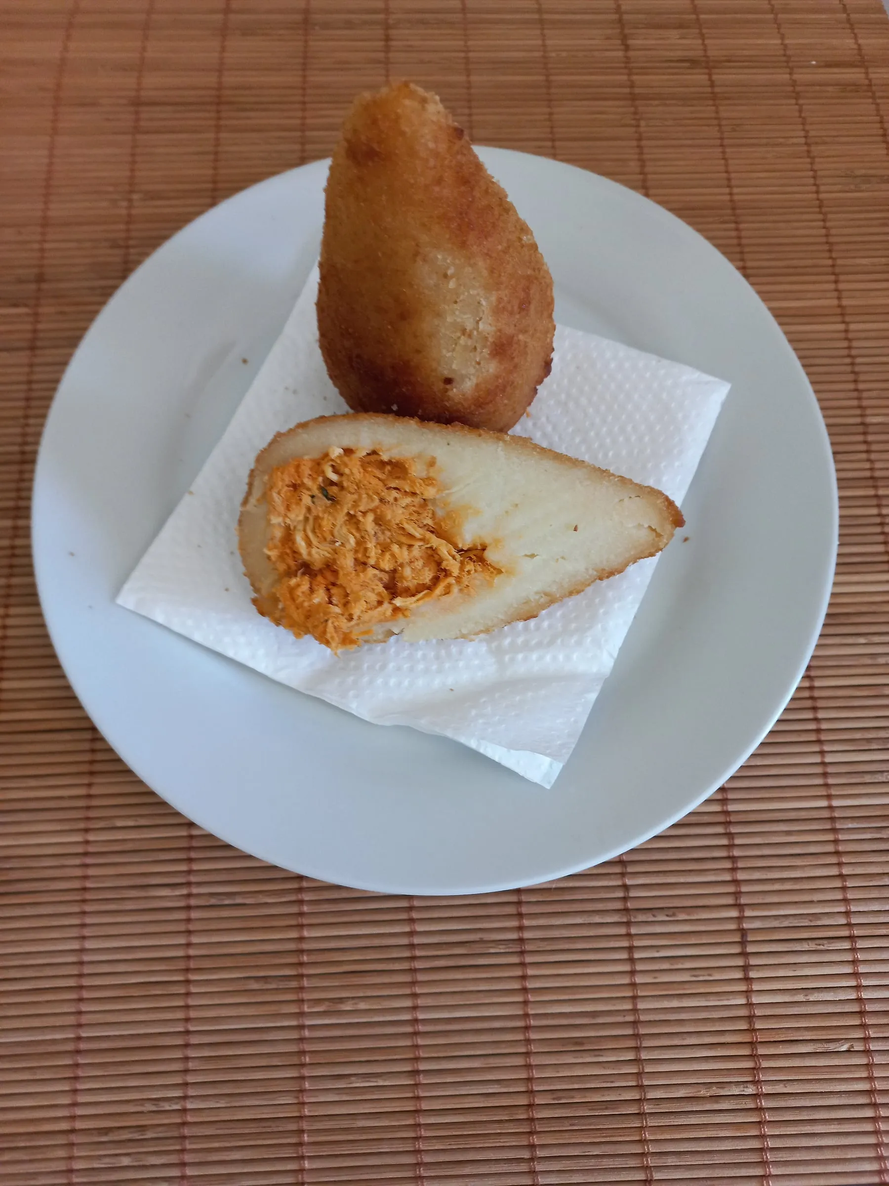 Coxinha panée frite garnie de poulet effiloché, illustrant coxinha au manioc, mini pastel et bolaço prêts au four/airfryer. Alt: coxinha de poulet brésilienne pâte au manioc gros plan salés surgelés