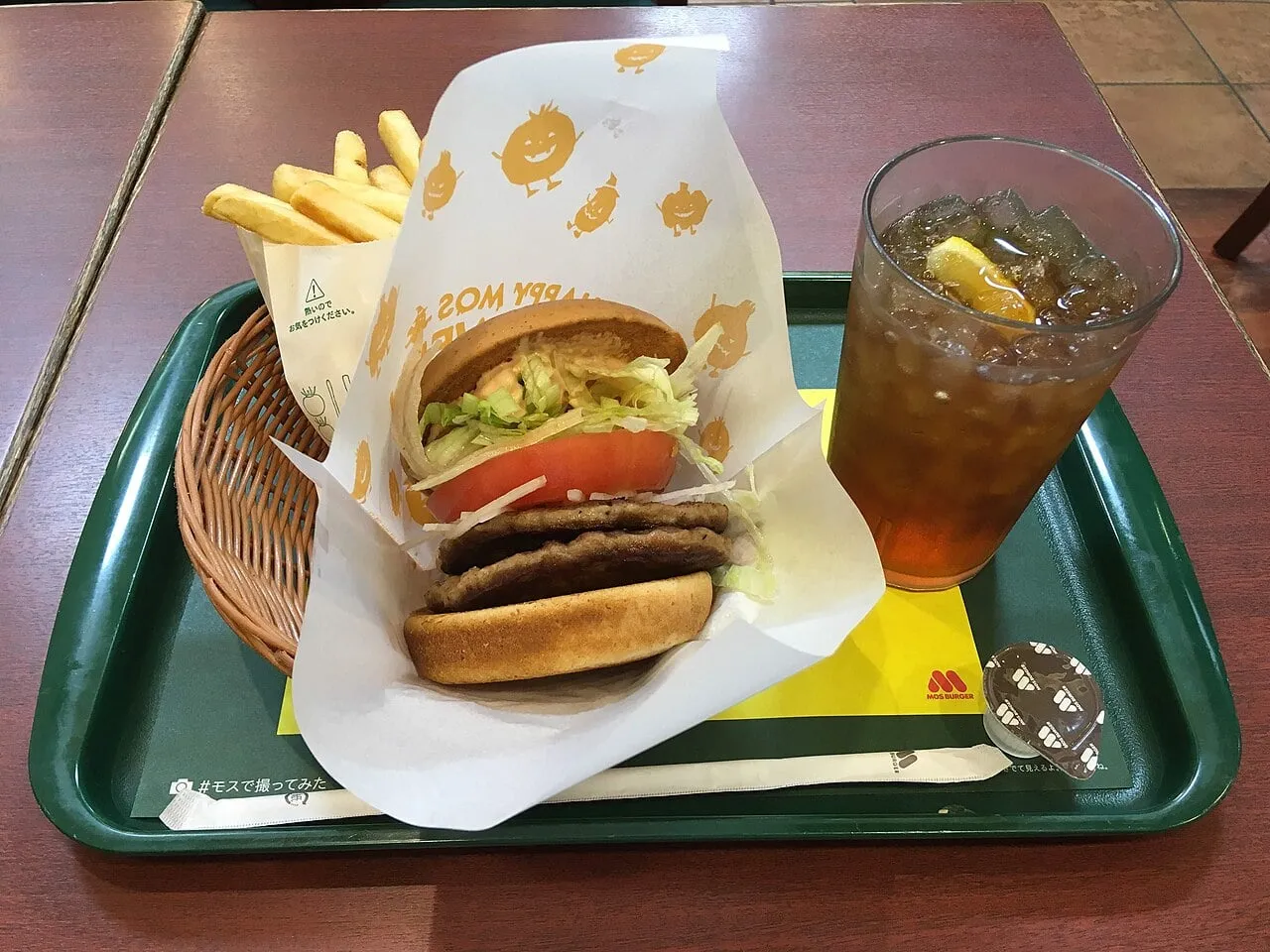 Menu MOS Burger à Hiroshima : burger à double steak avec tomate et laitue dans son papier, frites et thé glacé au citron sur un plateau vert MOS