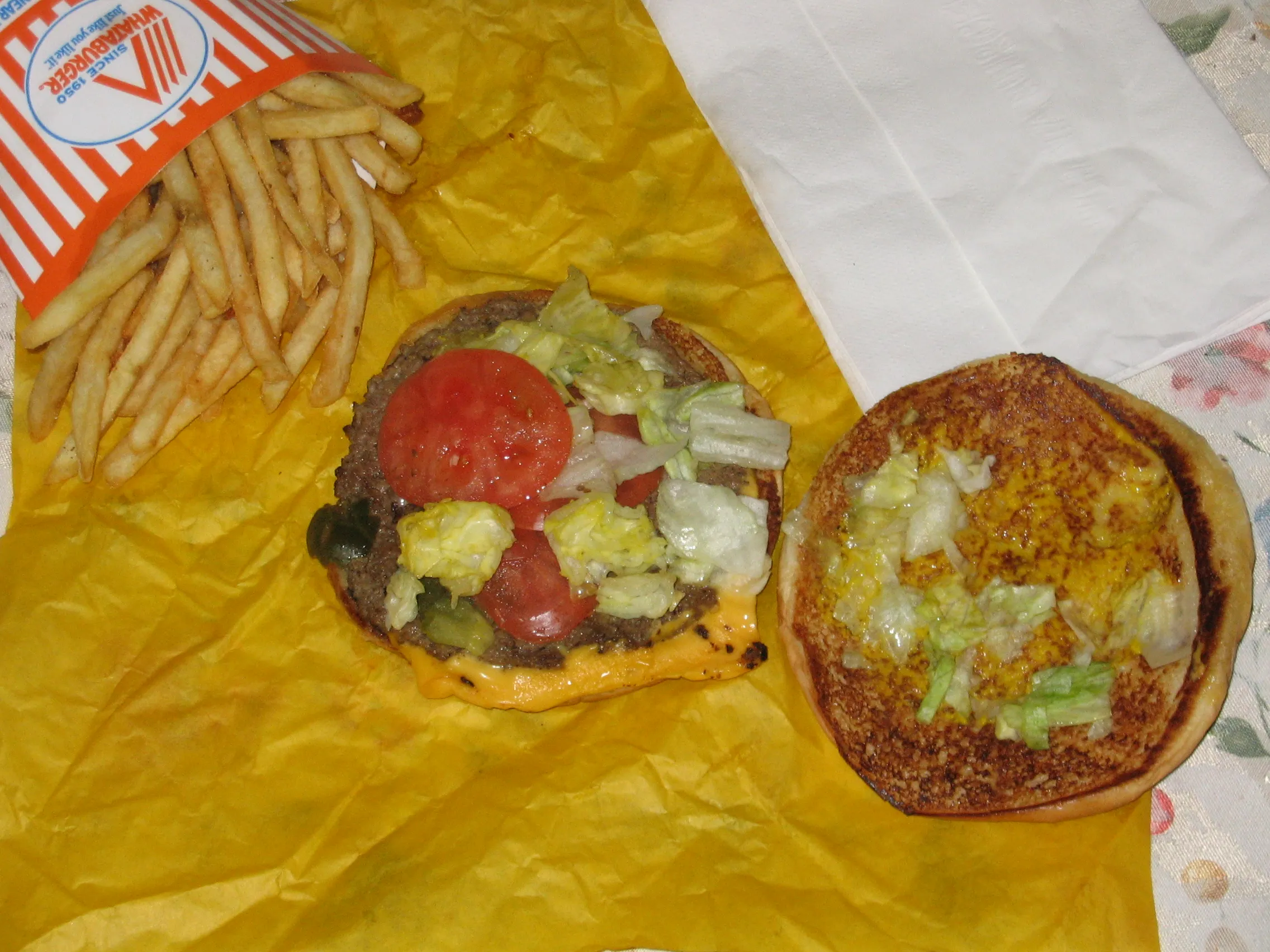 Open classic Whataburger showing the beef patty, mustard, lettuce, tomatoes and pickles on a toasted 5-inch bun
