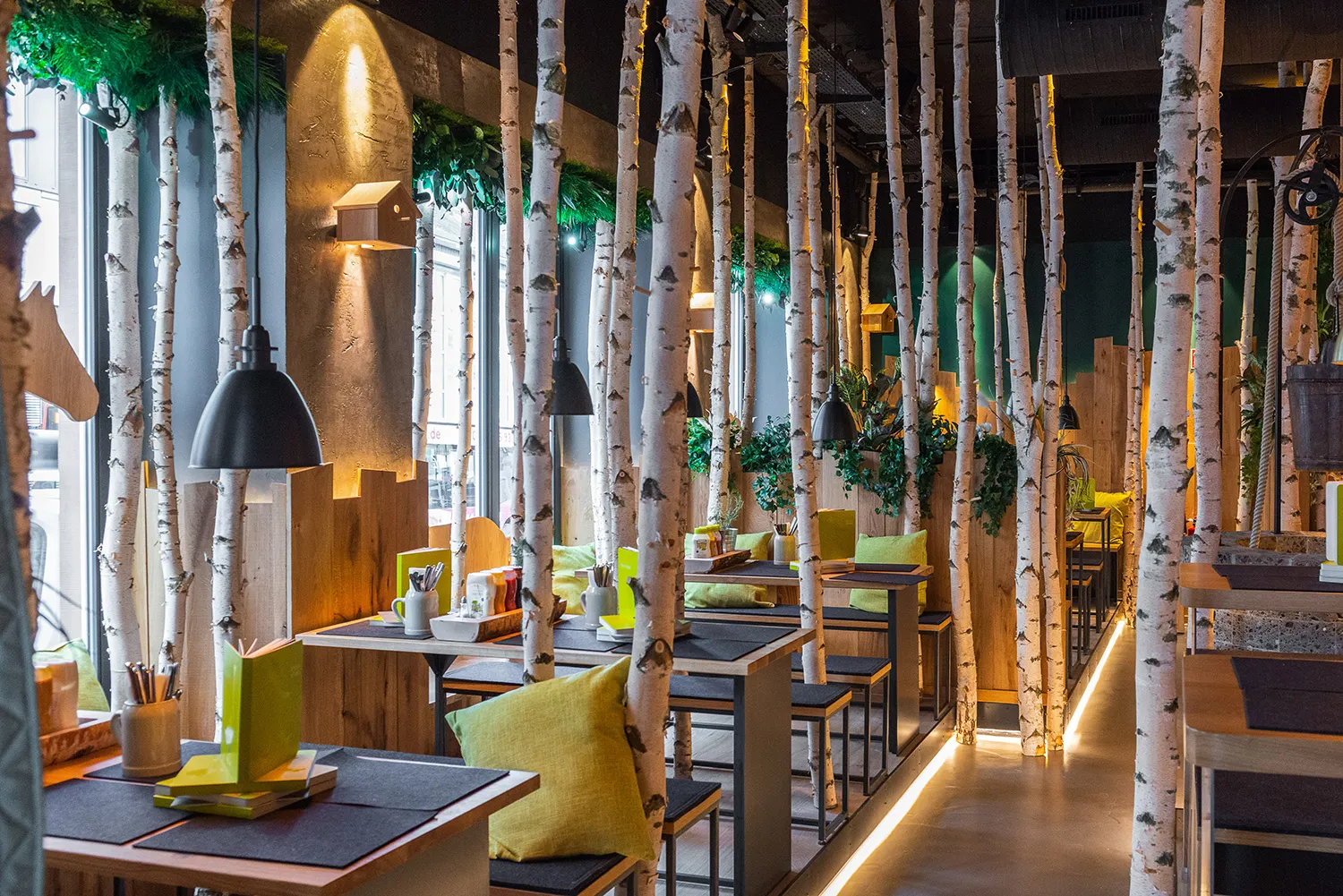Hans im Glück burger restaurant dining room with birch-trunk décor, wooden booths and green cushions