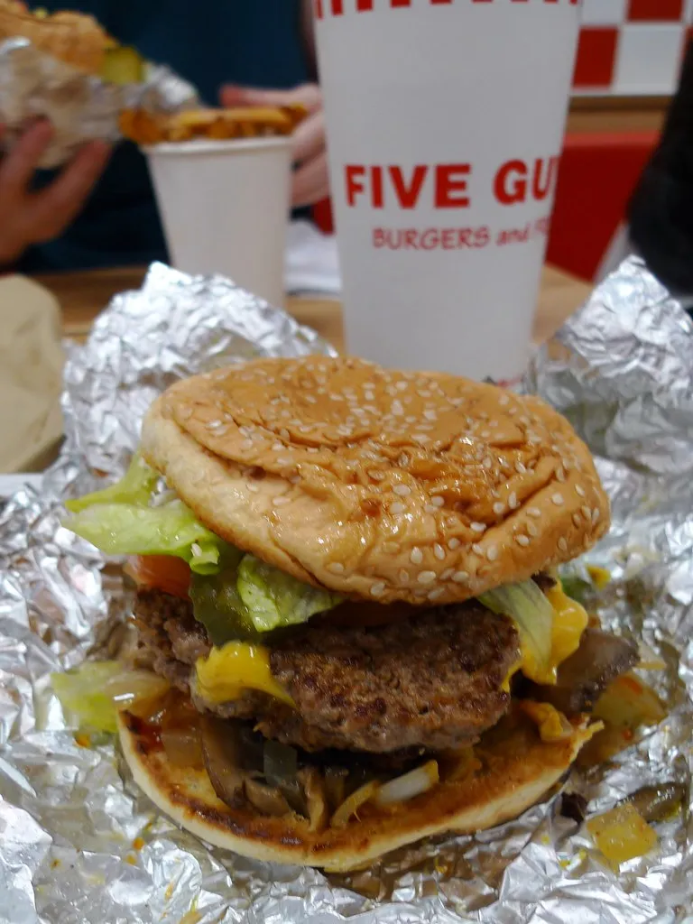 Five Guys cheeseburger with toppings in foil at Five Guys Covent Garden, London