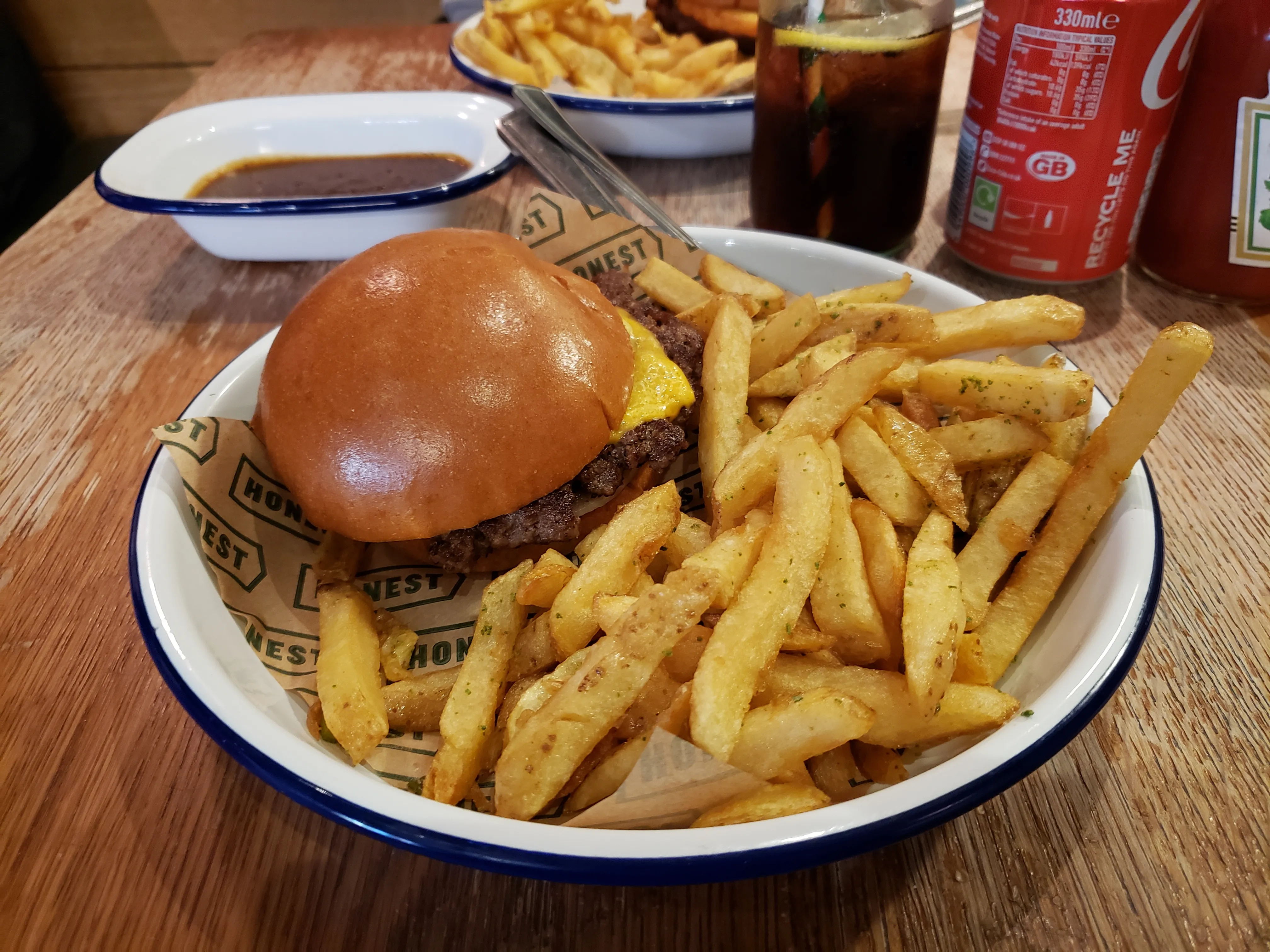 Single smash burger with American cheese on a brioche bun with fries, showing the thin browned crust of a smashed patty (photographed at Honest Burgers, not Junk Lyon)