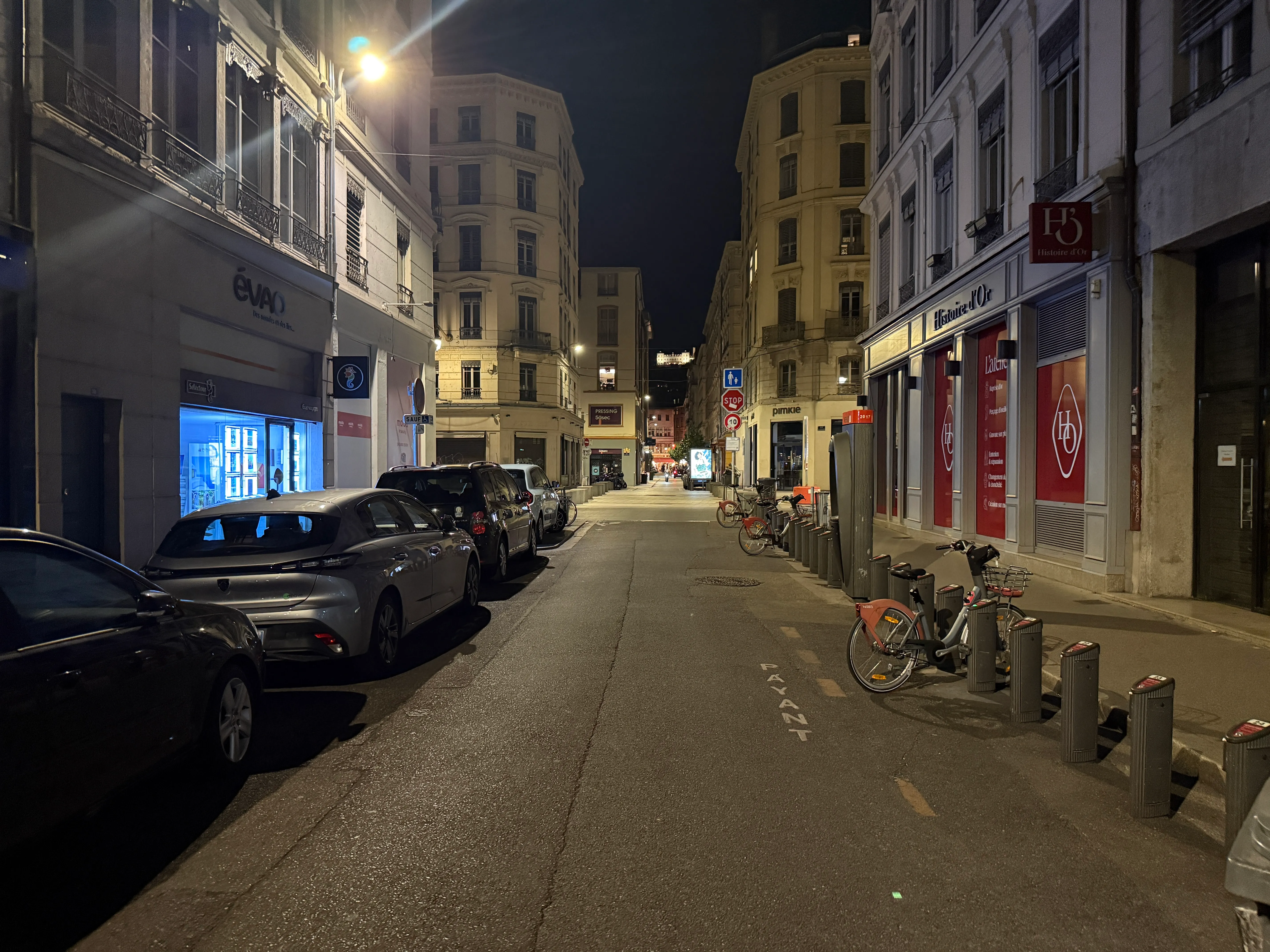 Rue Ferrandière in Lyon at night, the street of Junk Burger Lyon, with parked cars and a Vélo’v station