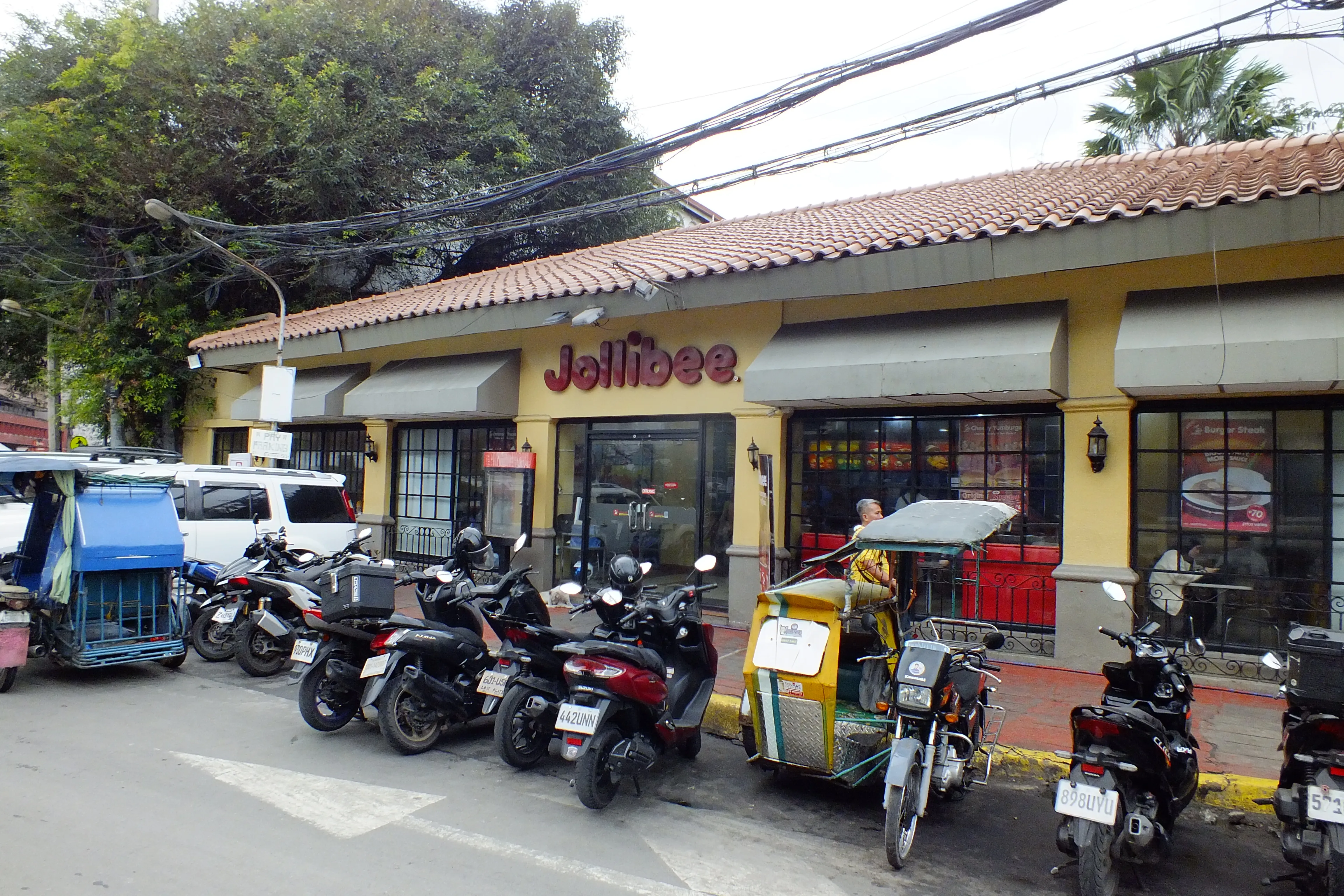 Jollibee in Intramuros, Manila, a low building with a terracotta tile roof and motorbikes and a tricycle parked out front